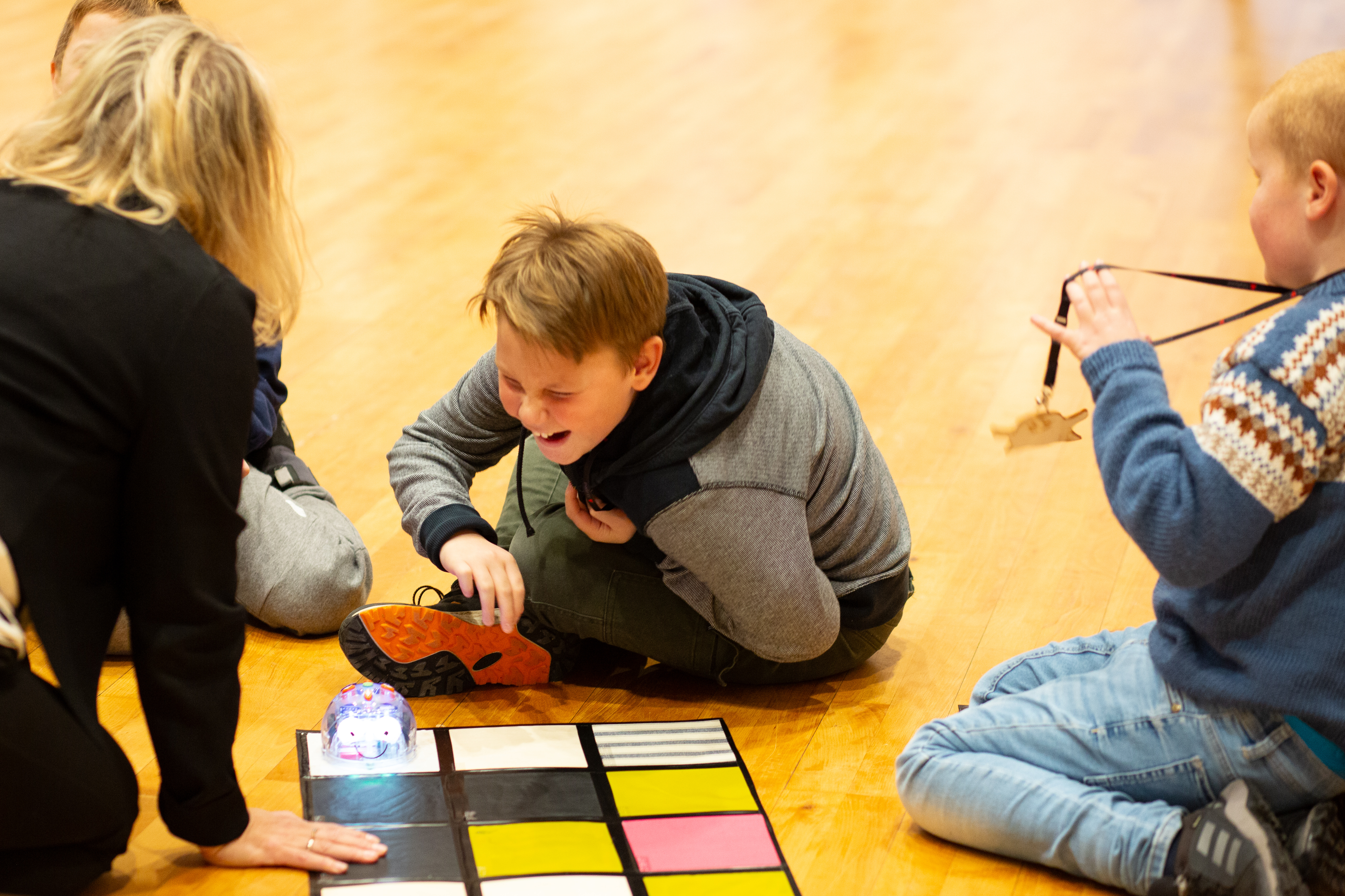 Elever som sitter på gulvet og programmerer en Blule-bot på et underlag.