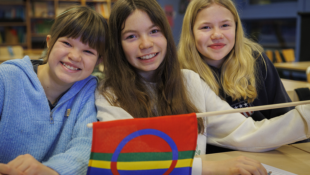 Tre jenter med det samiske flagget foran  seg.