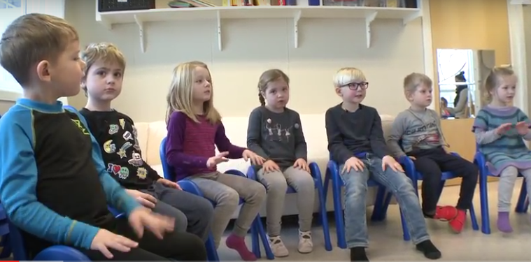Barn i en barnehage som sitter på stoler i en ring.