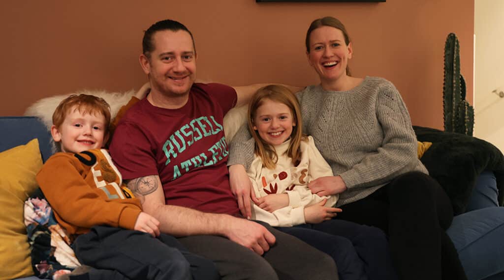 Familen til Emma sitter i sofanen. Bror, far, Emma og mor