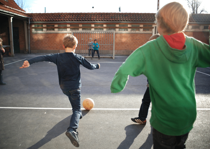 Gutter som spiller fotball i skolegård