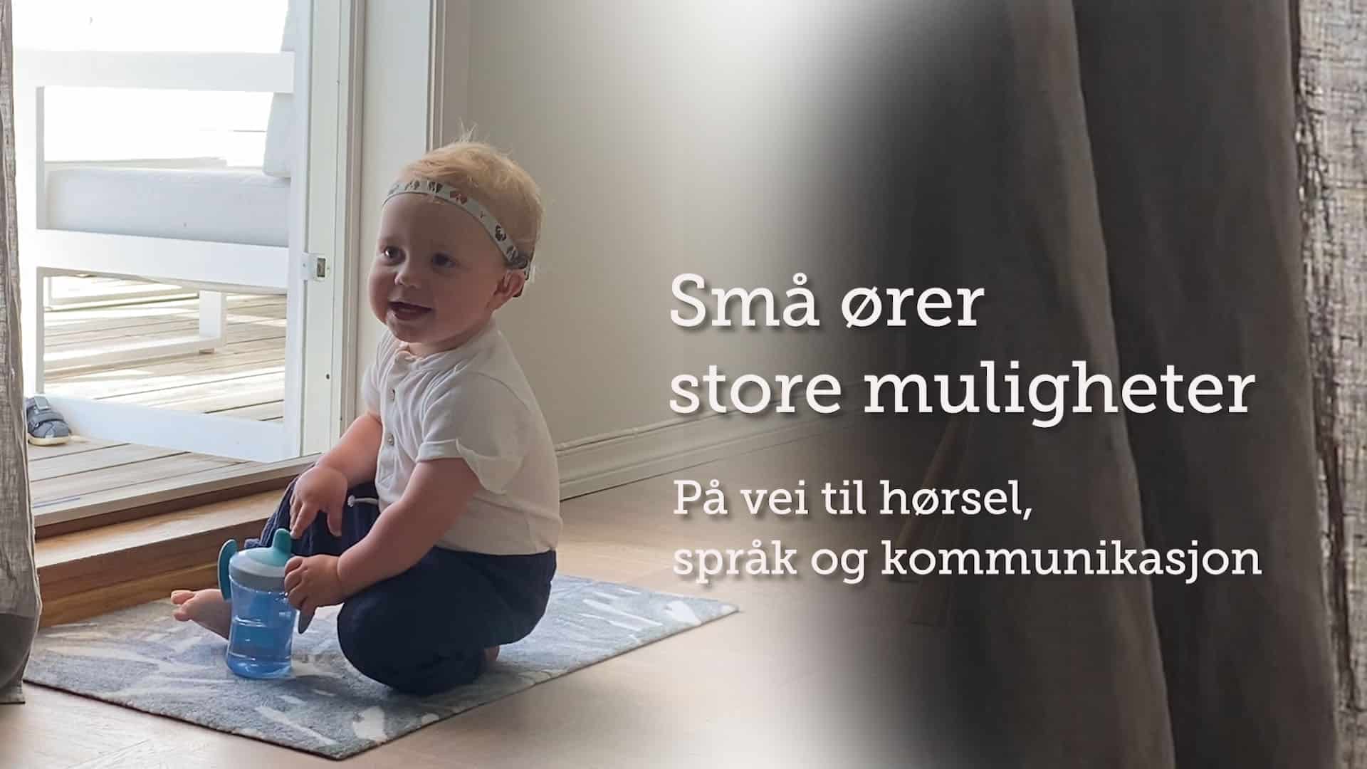 Tidemand (1) med CI sitter på en matte med drikkekopp. Tekst: "Små ører store muligheter. På vei til hørsel, språk og kommunikasjon"