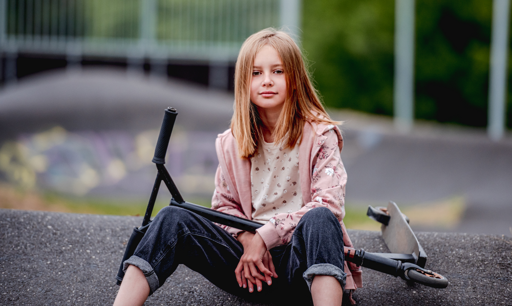 Jente sitter på bakken med sparkesykkel i skatepark