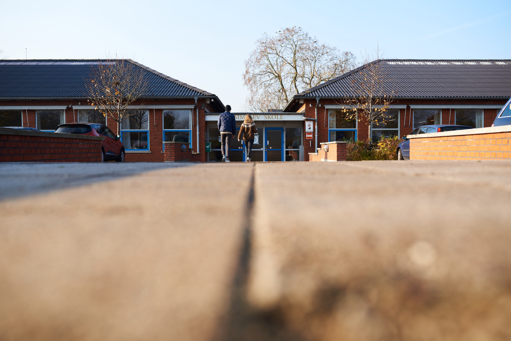 voksen og barn langt unna, forran skolebygg