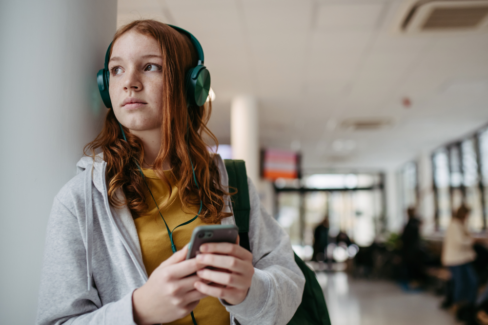 jente med hodetelefoner og mobil i gang på en skole