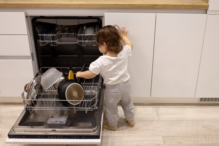 Liten jente som åpner en oppvaskmaskin og begynner å ta ut det som er inni.