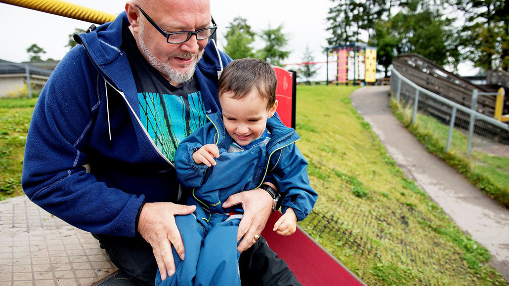 Gutt sitter på fanget til assistent utendørs i barnehagen