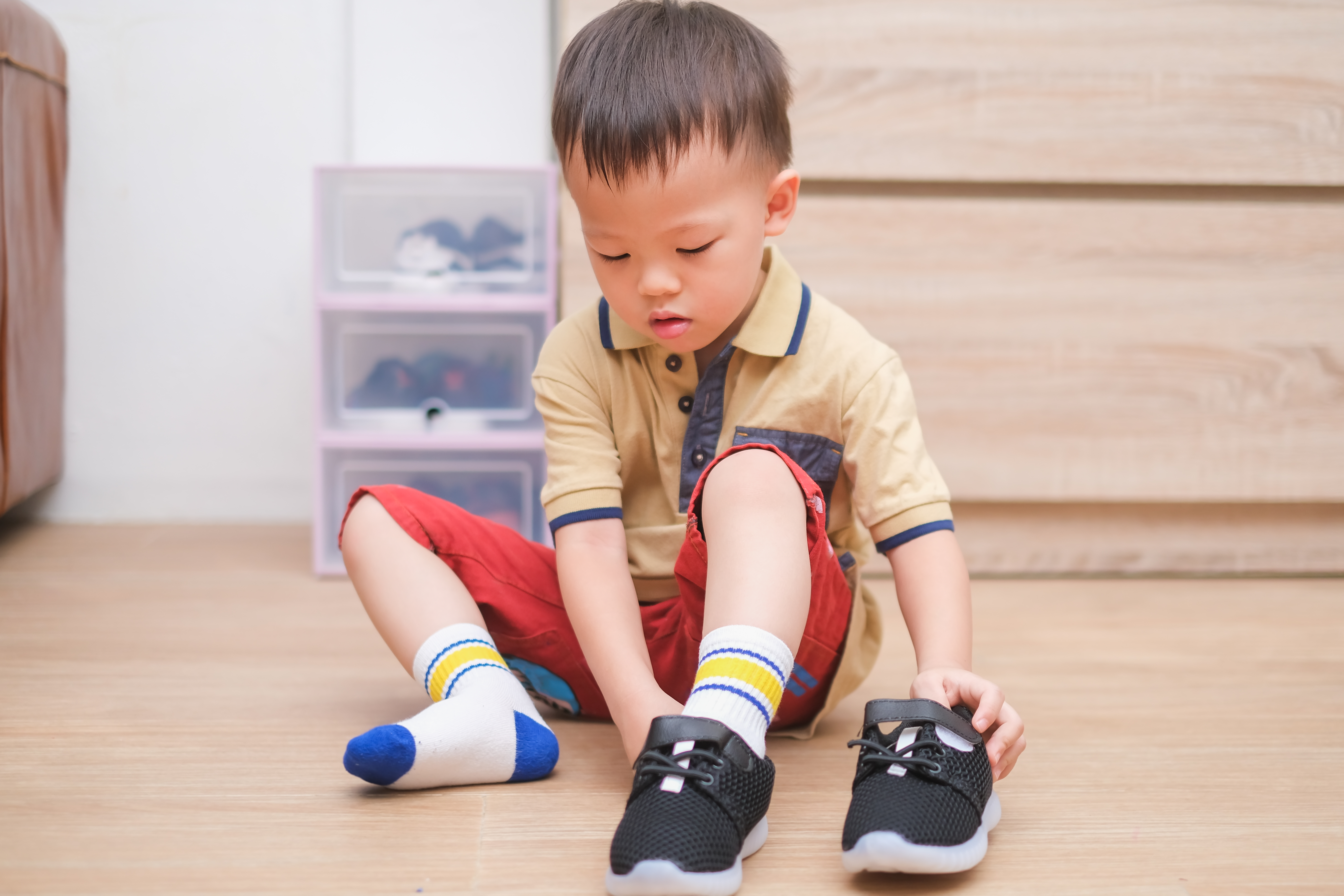 Liten gutt som tar på seg sko mens han holder en hånd på foten som har på seg skolen og den andre hånden på den andre skoen