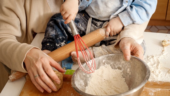 Baby som sitter på en kjøkkenbenk og hjelper med å røre i en bakebolle. En voksen holder rundt babyen.