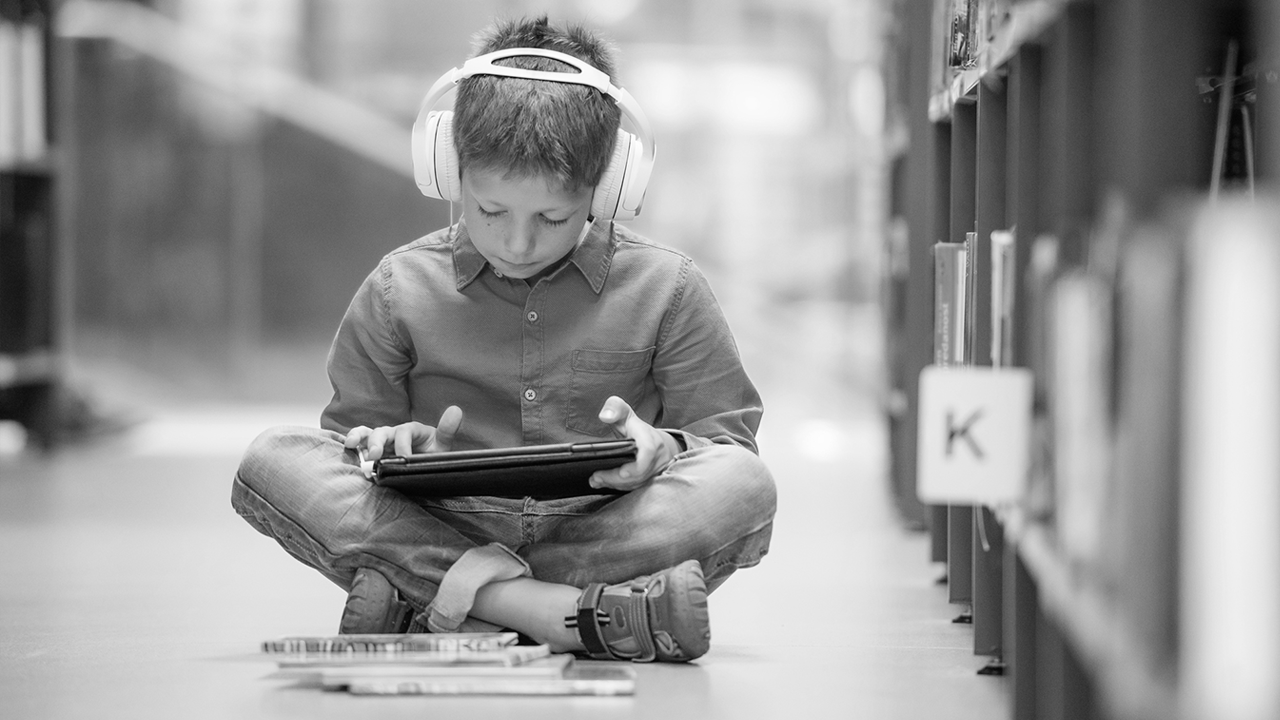 Gutt leser skolelydbok med hodetelefon og iPad.