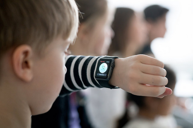 Et barn som sitter i klassen og ser på klokken han har på armen.