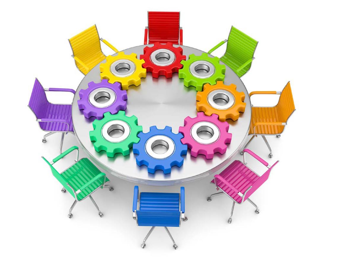 Stoler i ulike farger rundt et rundt bord. Det ligger tannhjul oppå bordet s om henger sammen i en sirkel