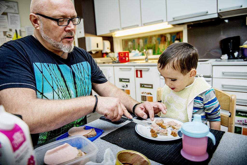 Mann skjærer brødskive i biter for liten gutt