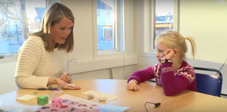 En logoped sitter sammen med et barn ved bordet og spiller kort.